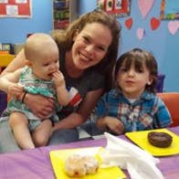 Adult holding a baby next to a child at a table with donuts