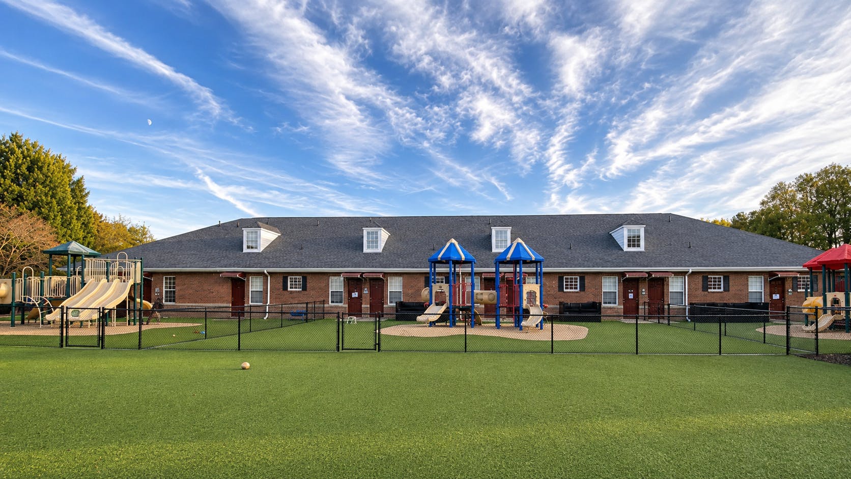 Playground equipment outside a long brick residential building under a blue sky