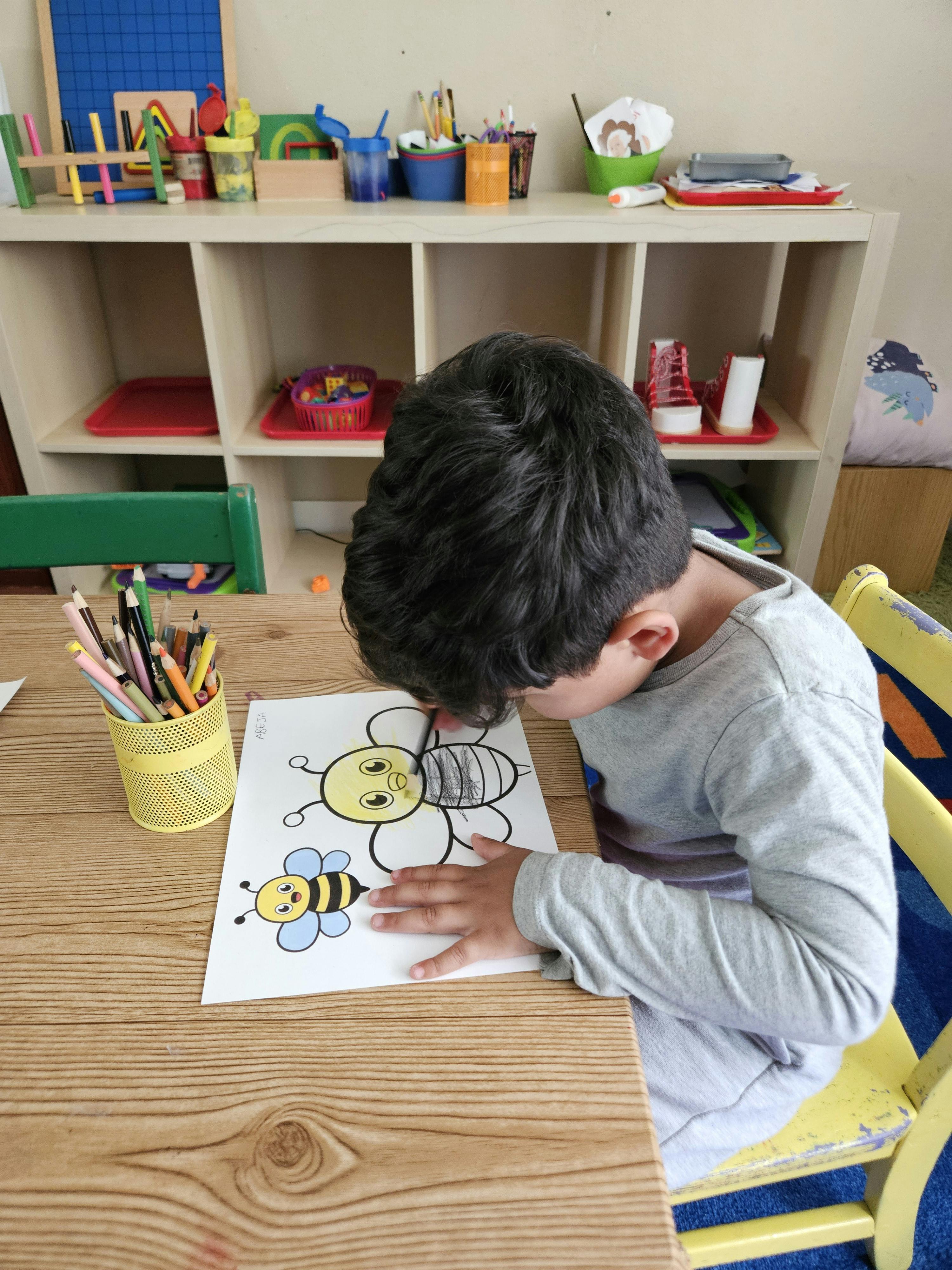 Child coloring a picture of a bee and flower at a table