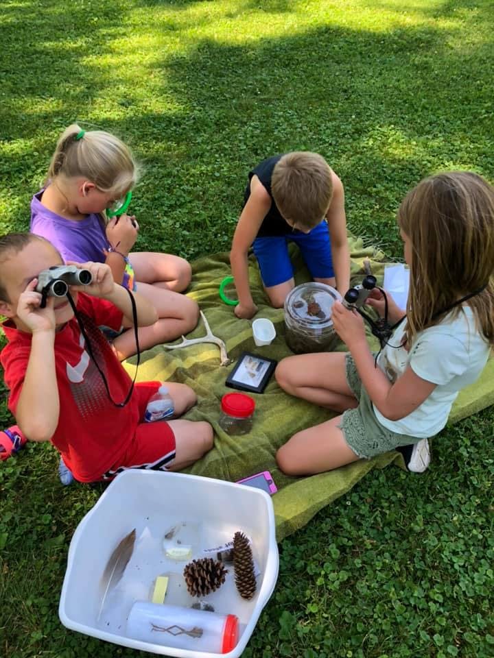 Children on a blanket on grass looking at nature items