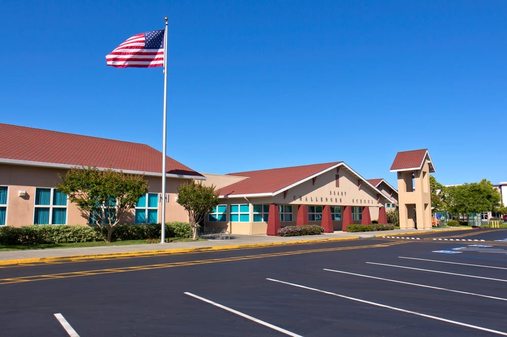 American flag flying in front of a school building with a parking lot