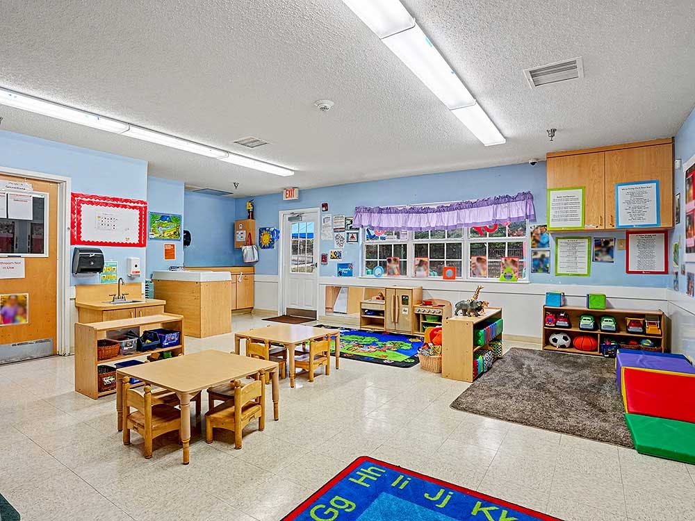 Classroom with small tables and chairs, play mats, and learning materials