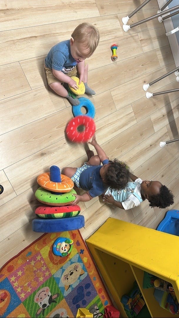 Three children playing with stacking rings on a wooden floor and colorful rug