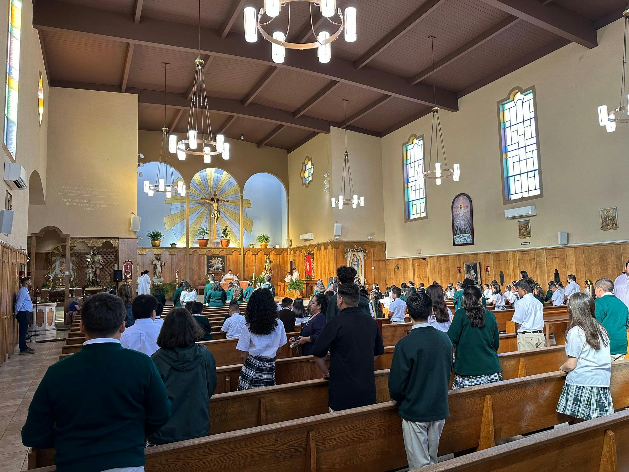 People in school uniforms standing in pews in a church