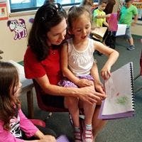 Adult and child reading a book together in a classroom