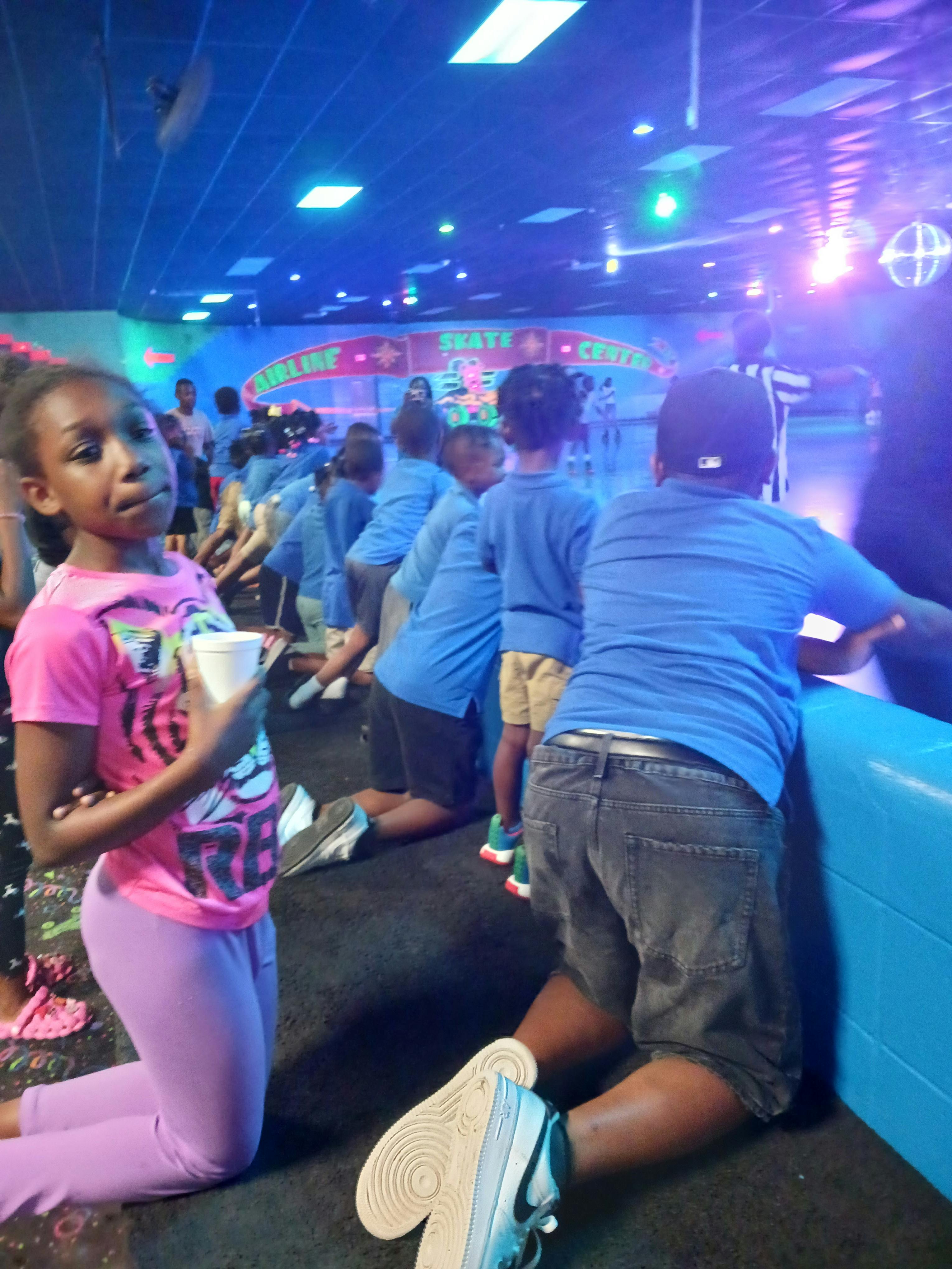 Child in pink shirt kneeling with a cup, other children kneeling in background
