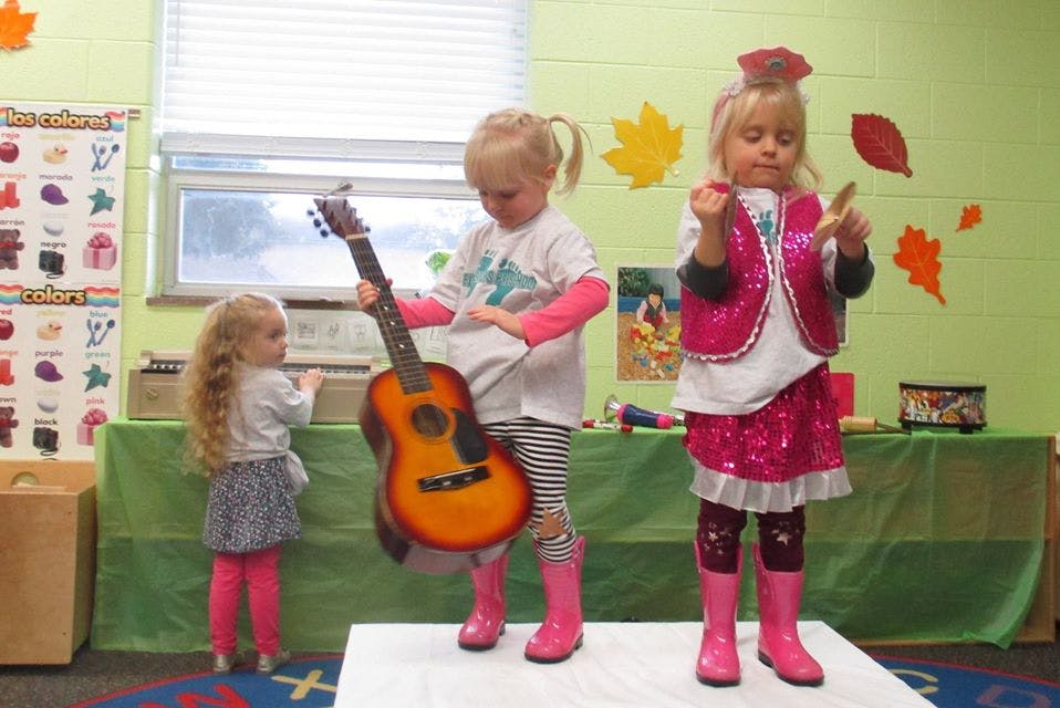Child holding a guitar next to another child in a sparkly outfit