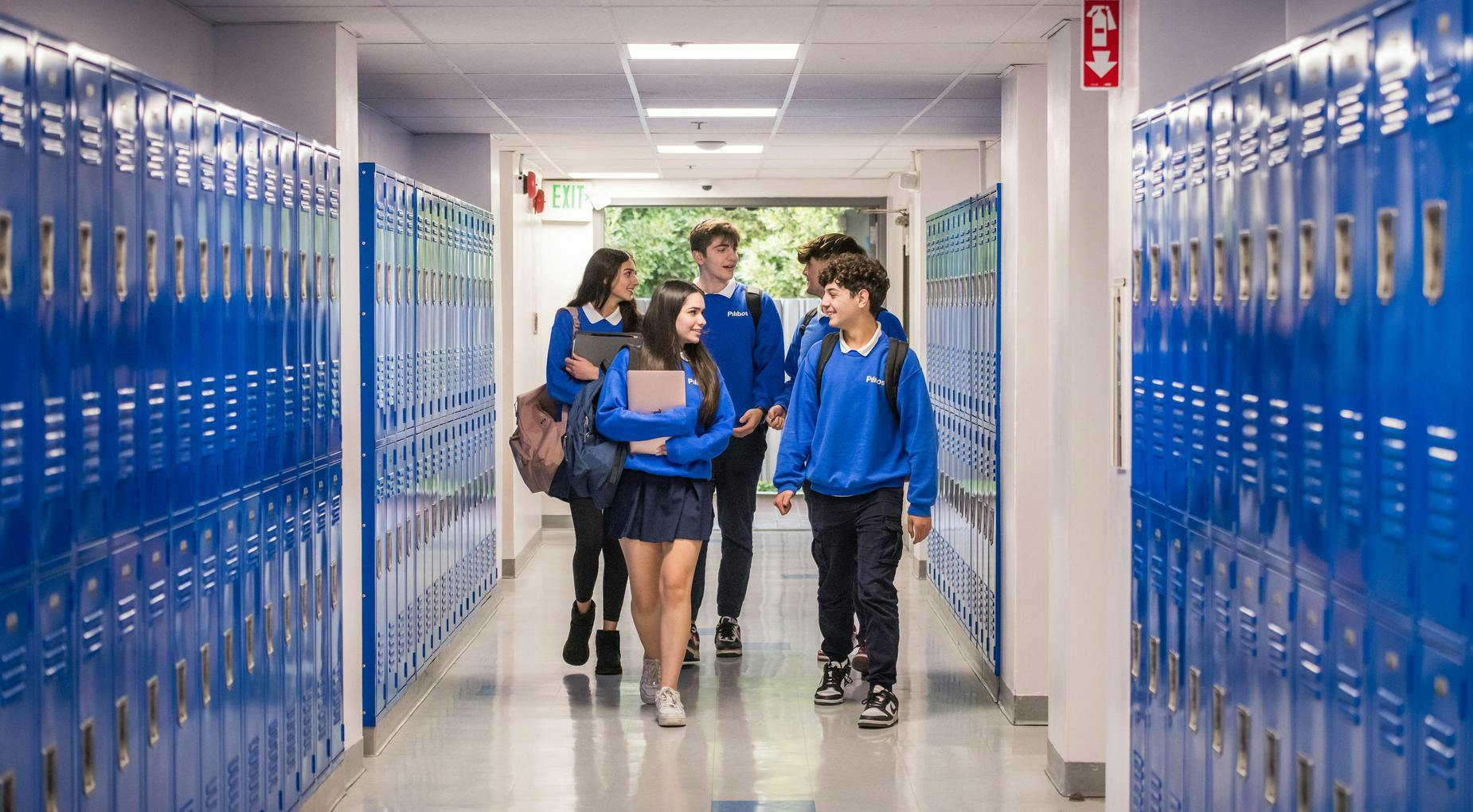 Five teens walking down a school hallway filled with blue lockers