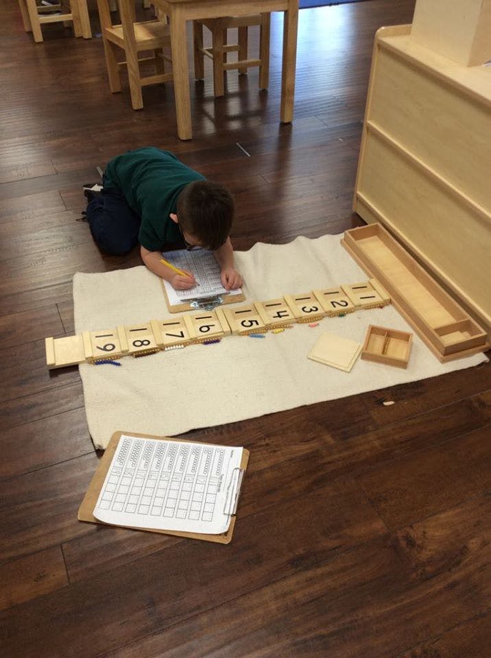 Child kneeling on floor writing on paper with number blocks