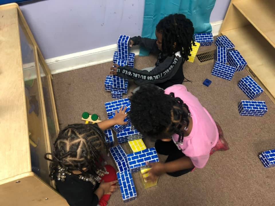 Three children playing with blue and yellow building blocks on the floor