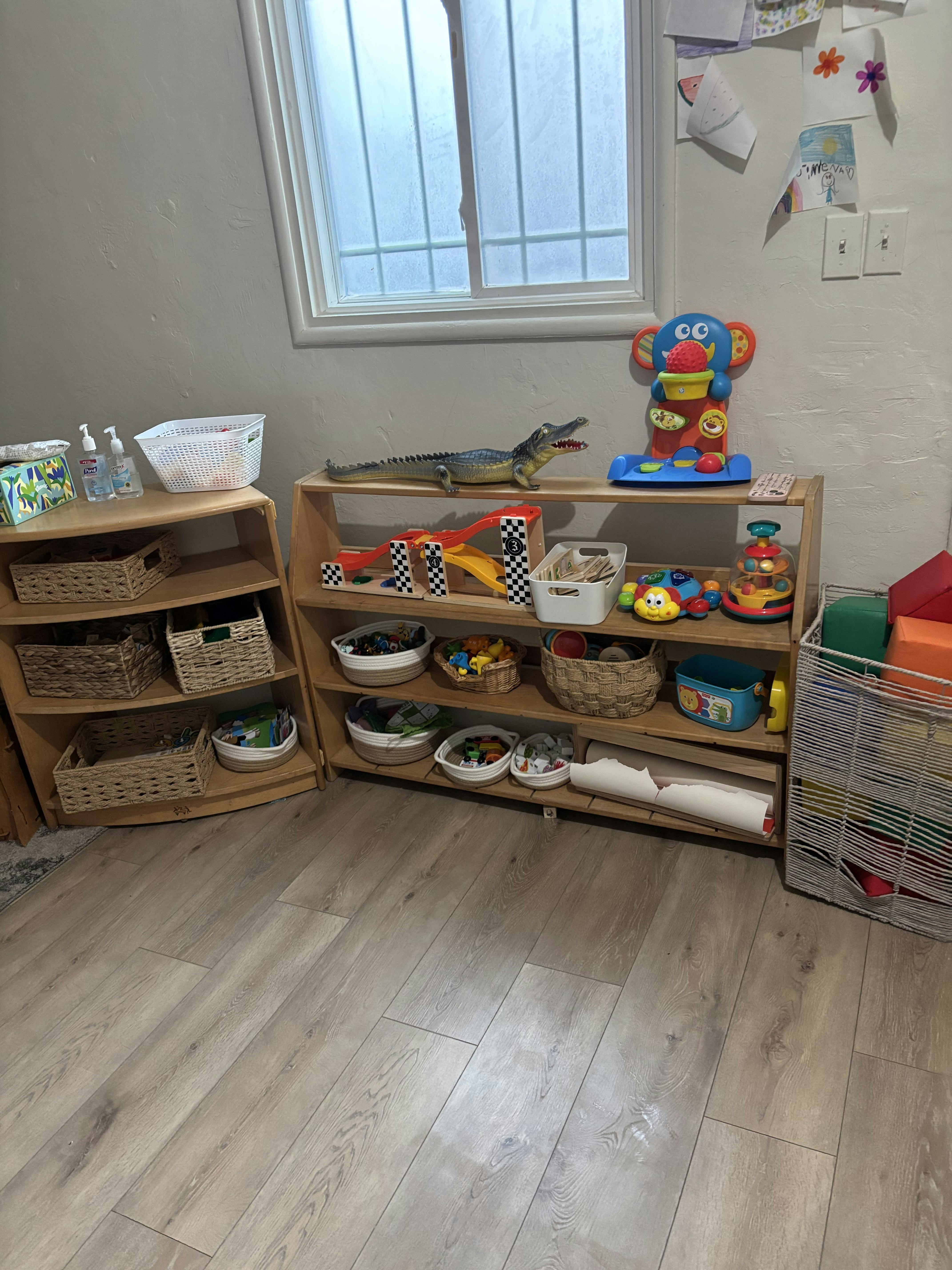 Classroom shelving with baskets of toys, a toy alligator, and children's drawings