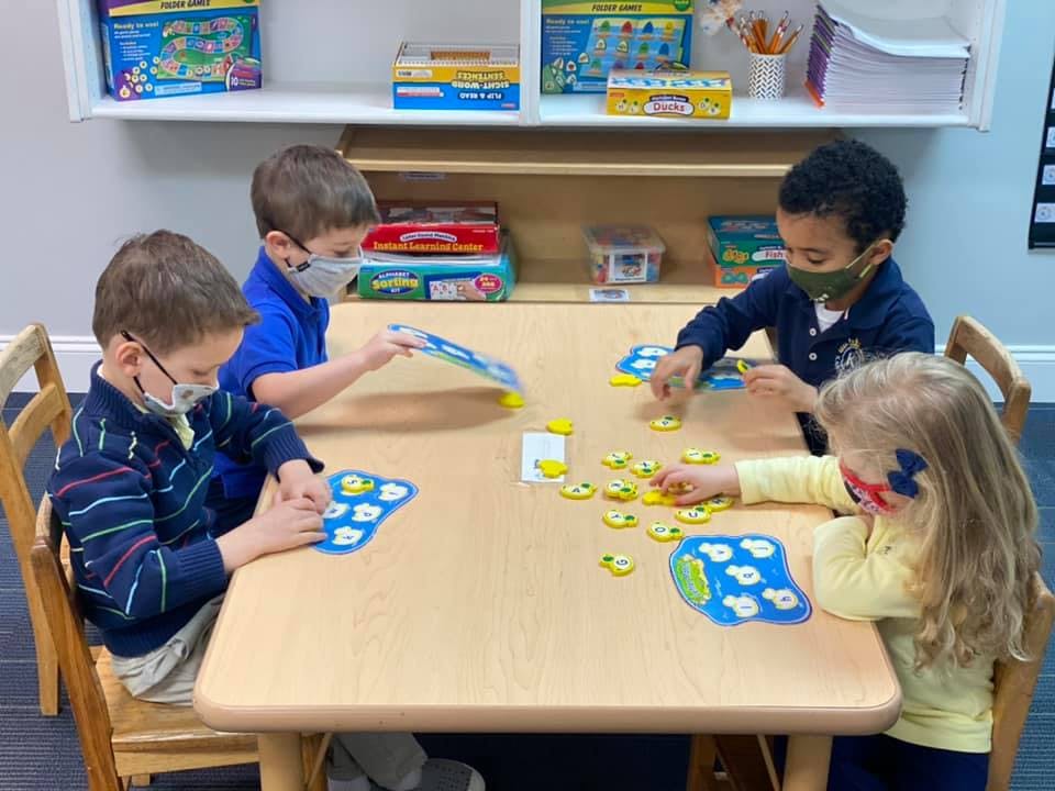 Four children wearing masks playing a board game at a table