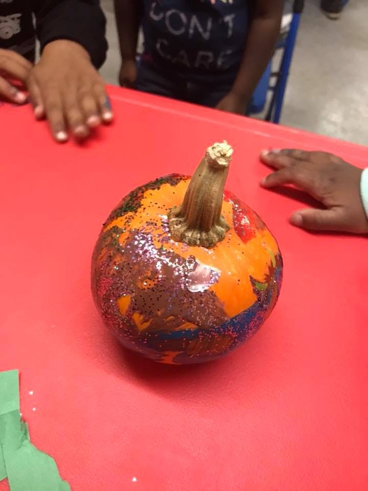 Decorated pumpkin on a red surface with children's hands nearby