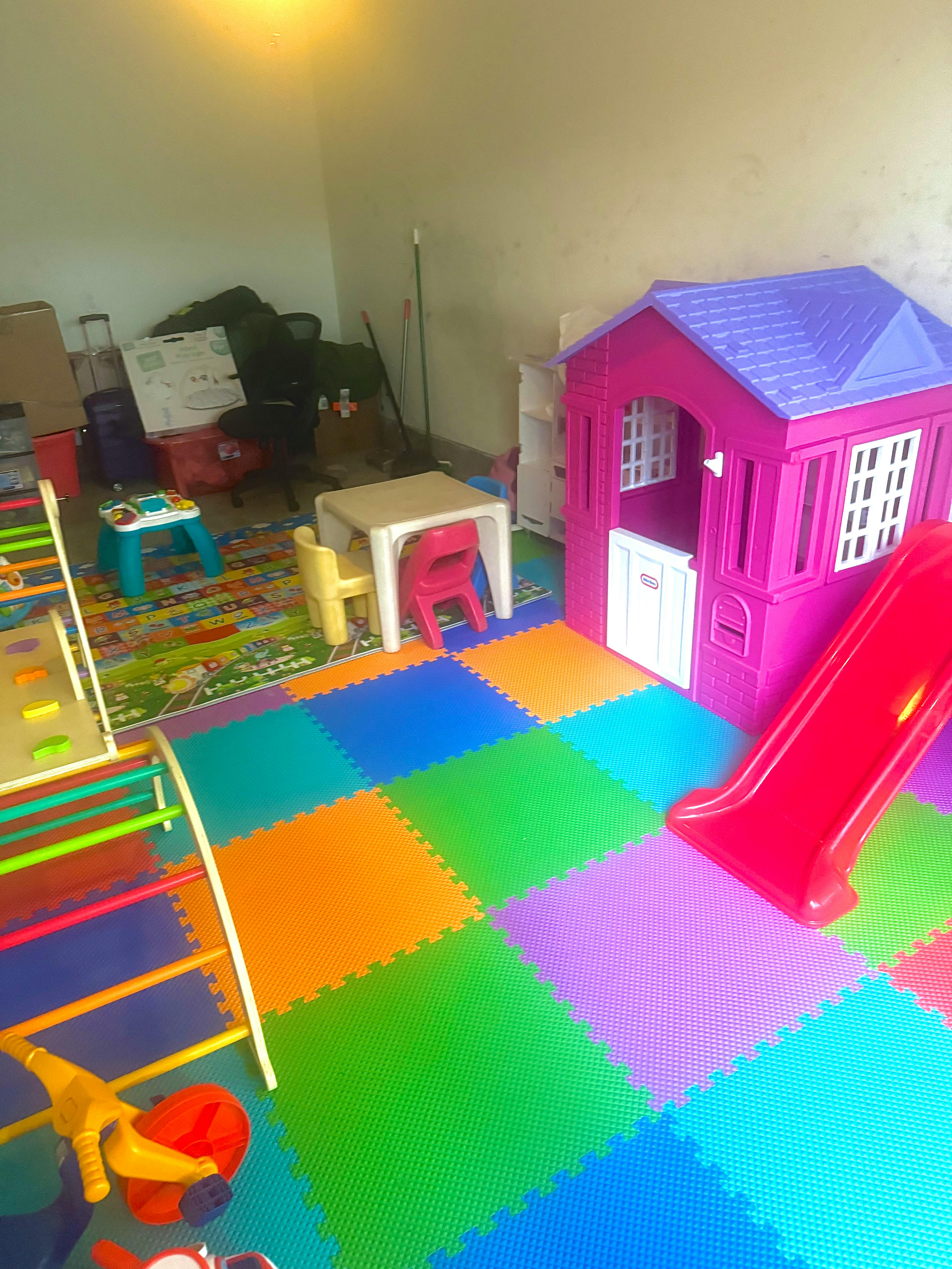 Playroom with colorful floor mats, a pink playhouse with a red slide, and a small table