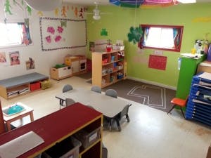 Classroom with small tables and chairs, shelves, and a whiteboard