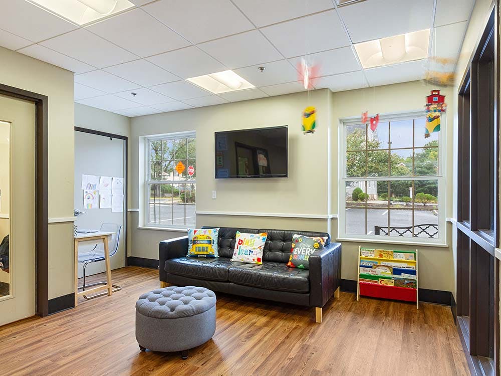Waiting room with a black couch, grey ottoman, TV, and bookshelf