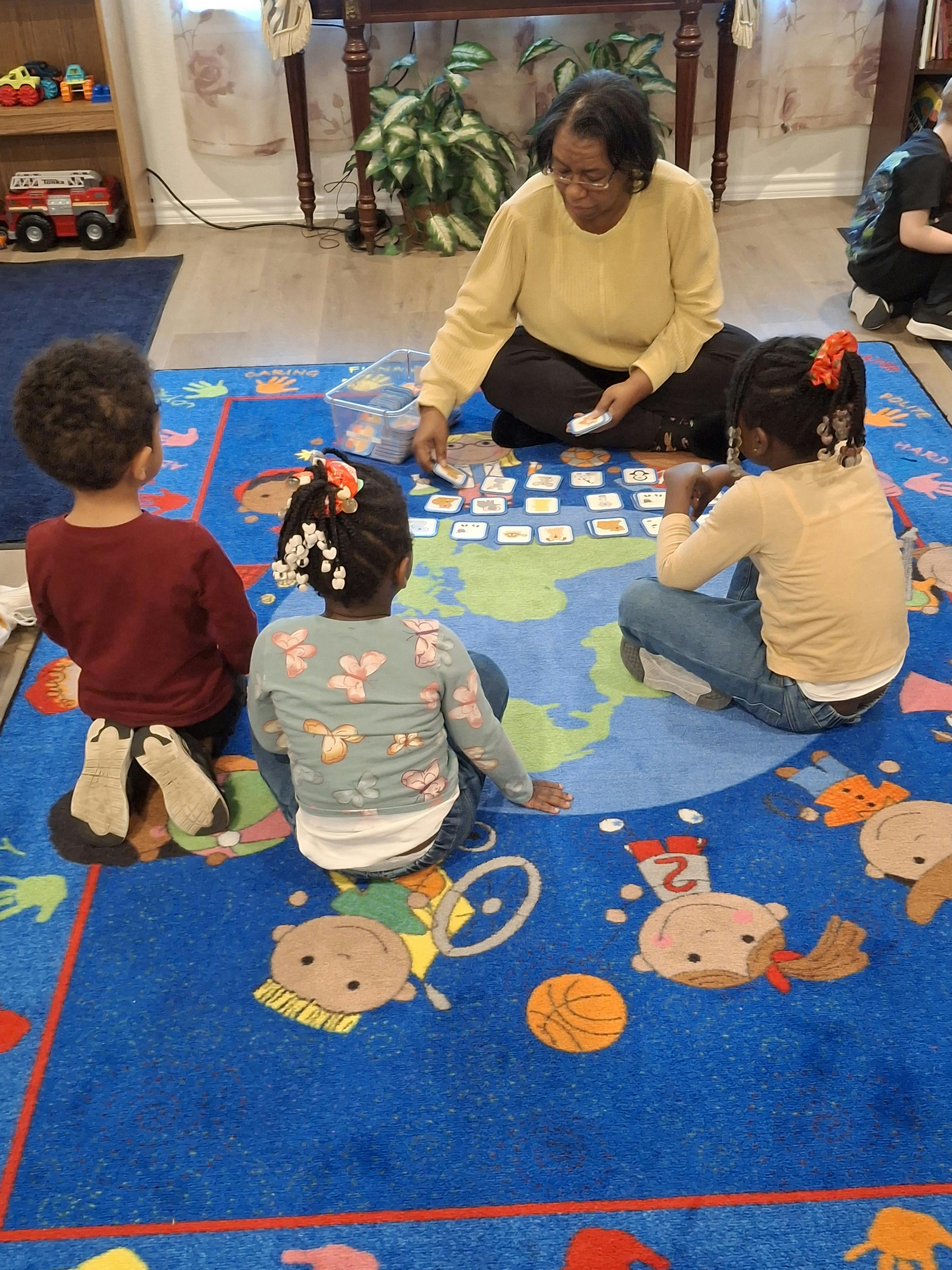 Adult and three children sitting on a rug playing a card game