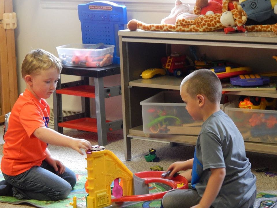 Two children playing with a toy car track on the floor