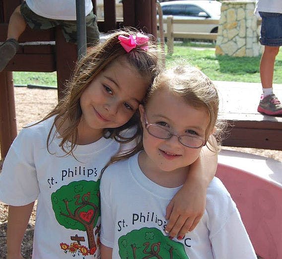 Two children in white shirts with a tree design, one with arm around the other
