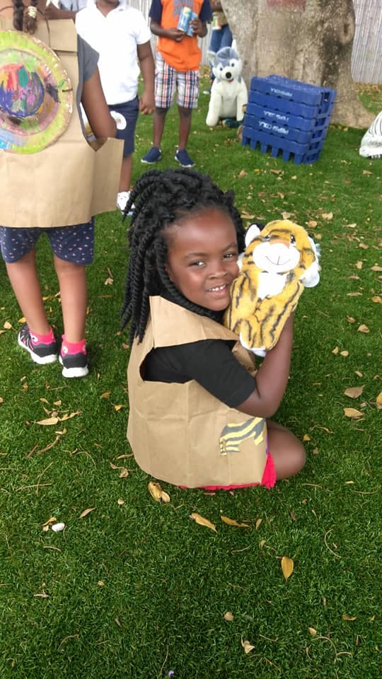 Child kneeling on grass holding a tiger puppet