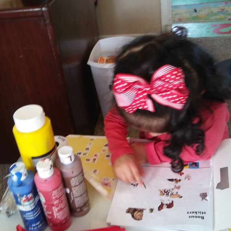Child with a large bow in hair looking at a sticker book