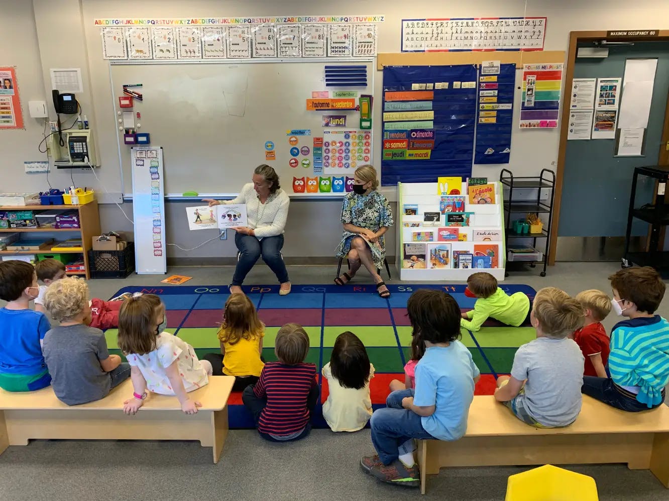 Two people reading a book to a group of children in a classroom