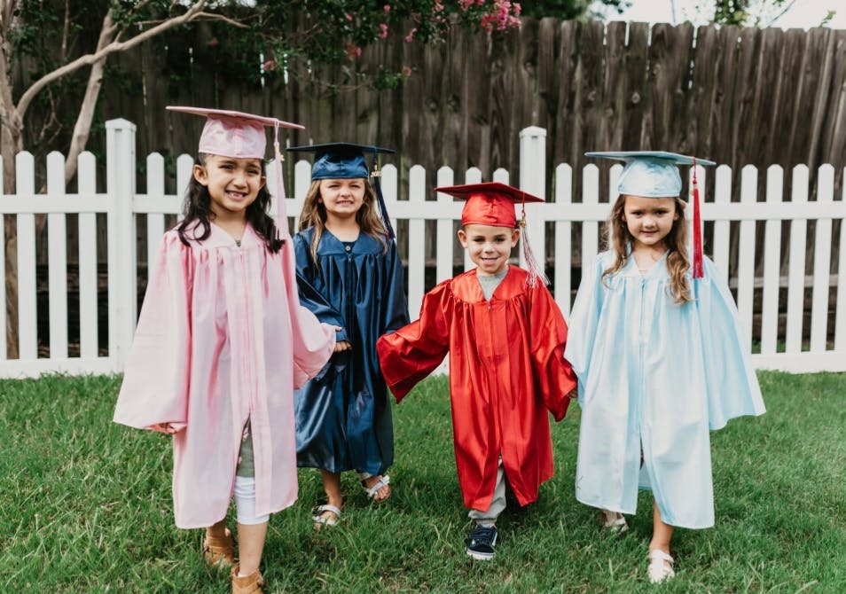 Four children in graduation caps and gowns standing on grass