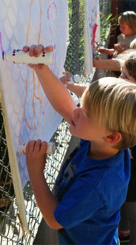 Child painting on a large white canvas outdoors