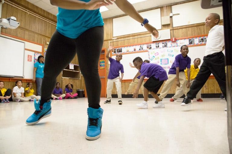 Person in blue shirt and black pants dancing with children in a classroom