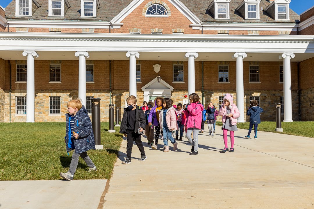 Children walking on a path in front of a large building with columns