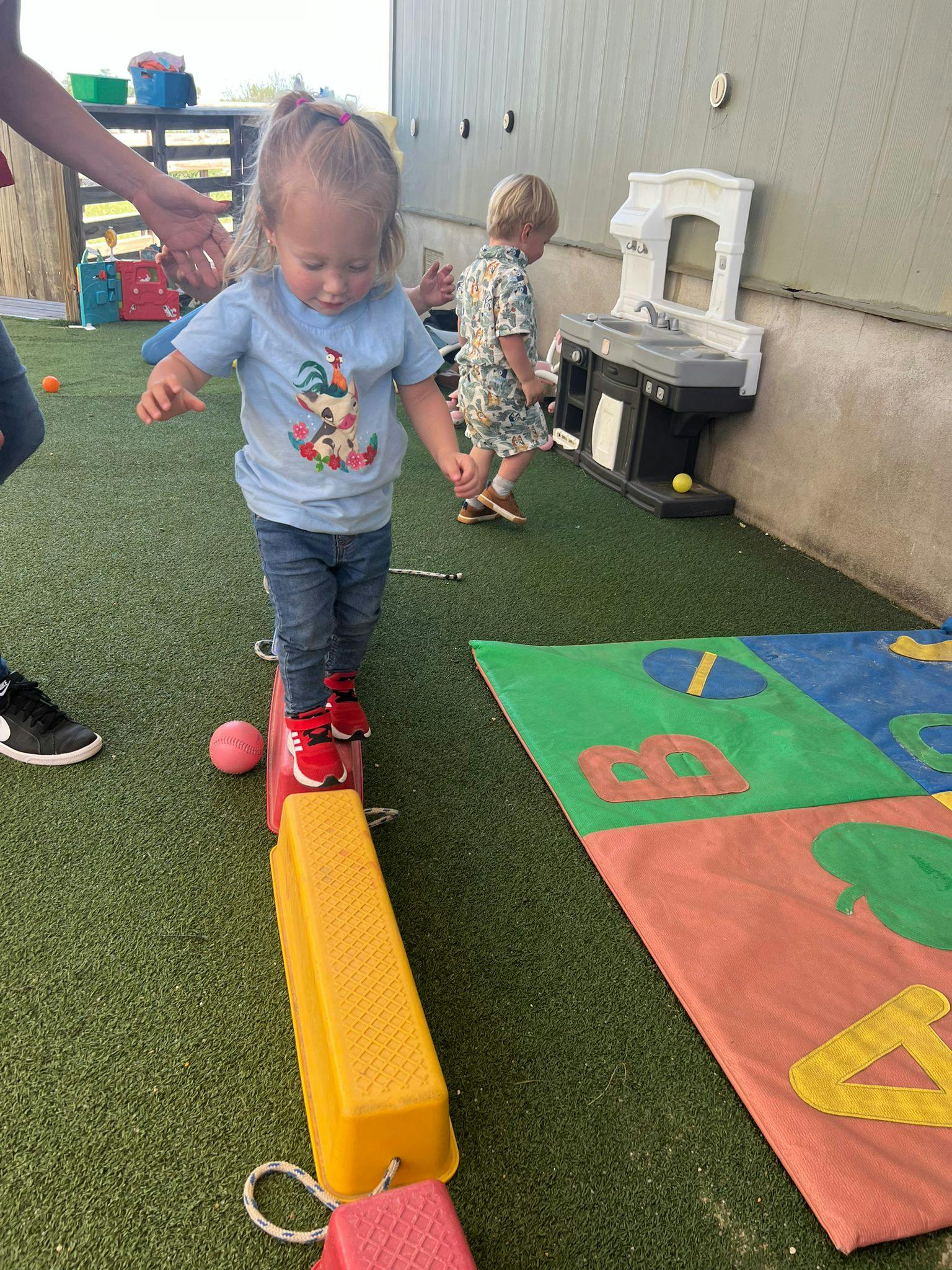 Child walking on a balance beam with another child in the background