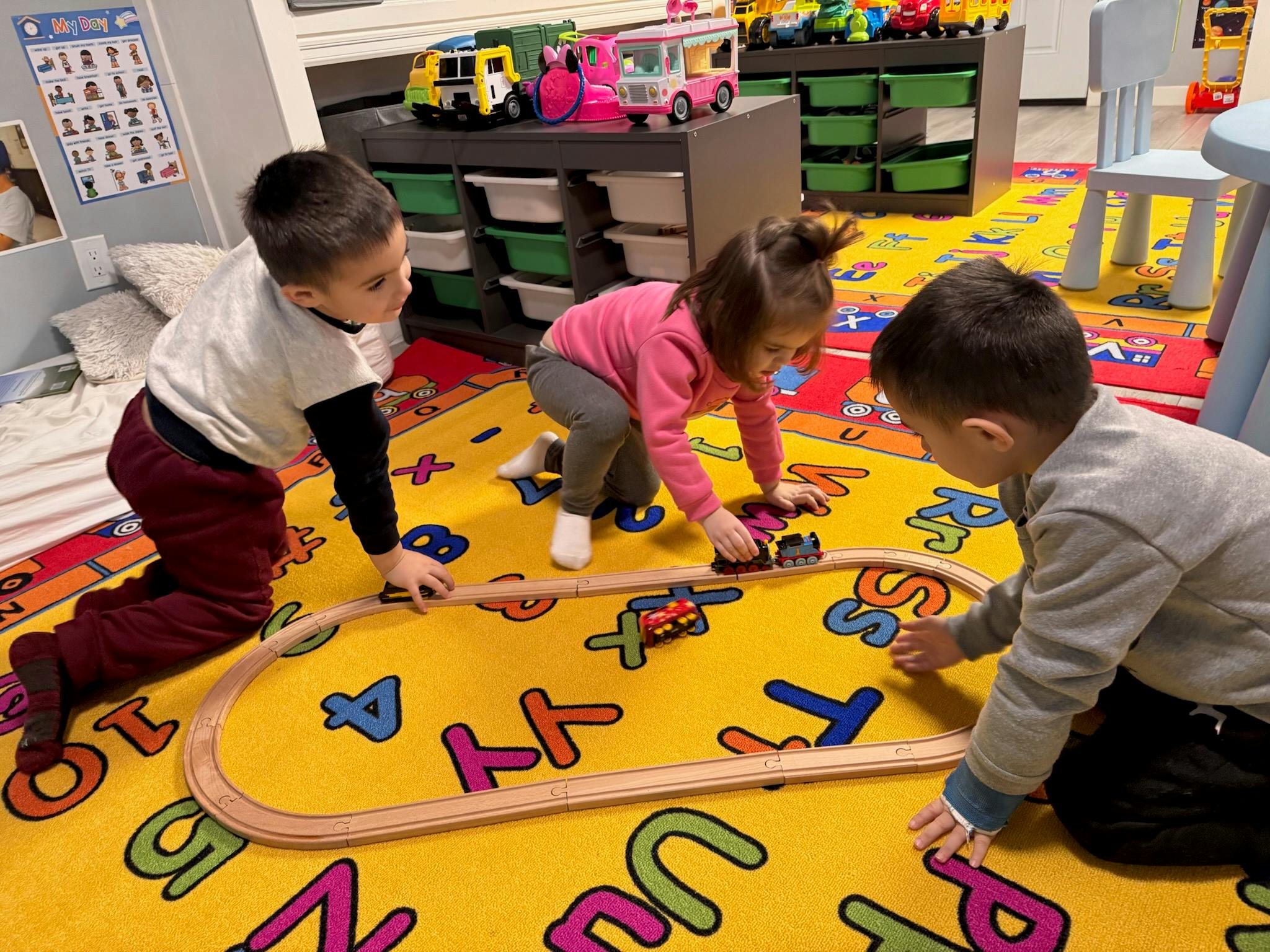 Three children playing with a toy train set on a colorful rug
