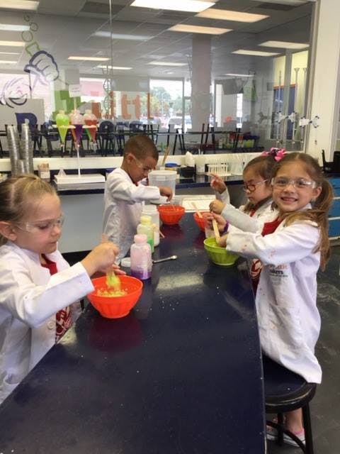 Children in lab coats mixing ingredients in bowls at a table
