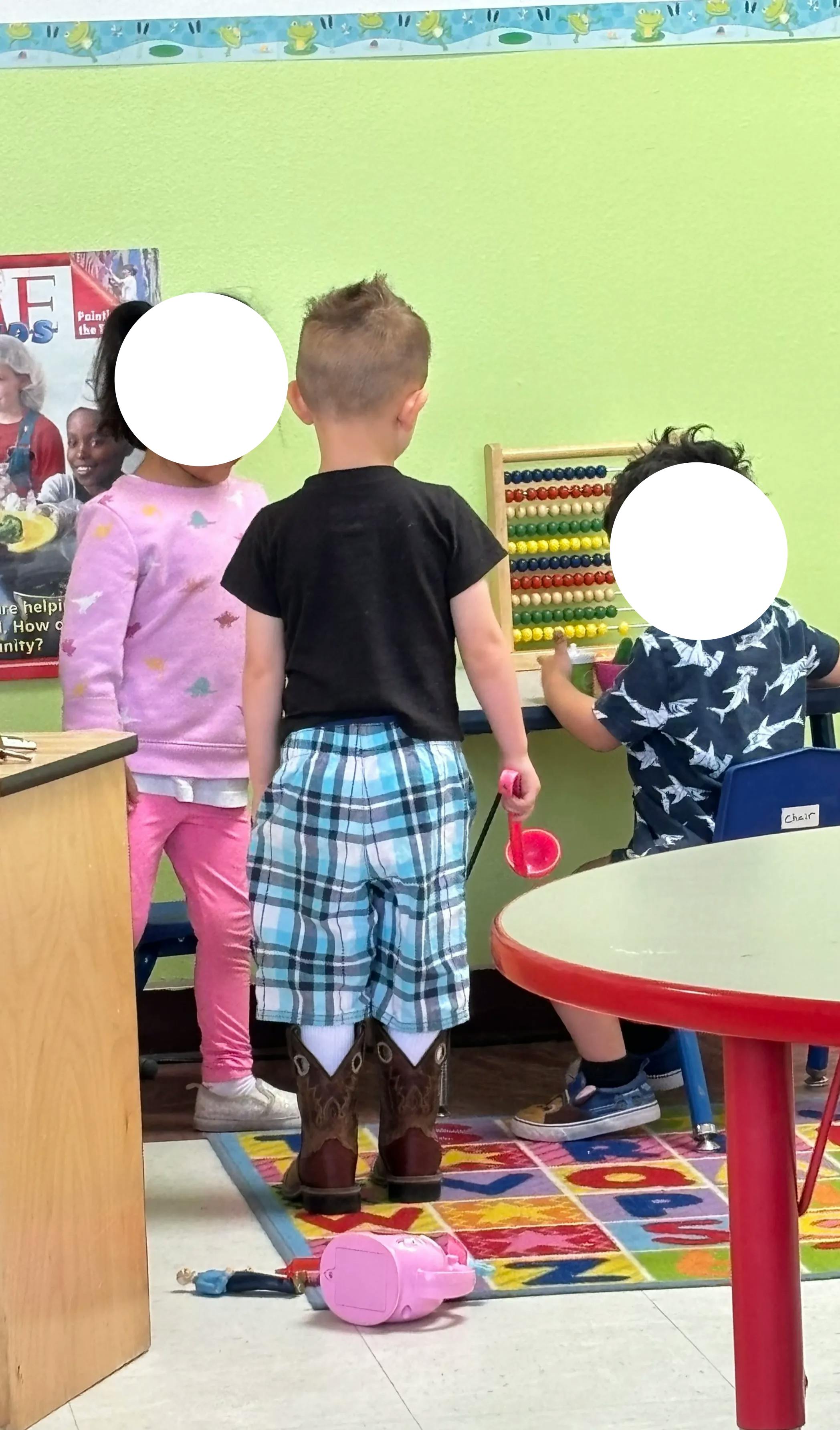 Children in a classroom, one child wearing cowboy boots and holding a toy