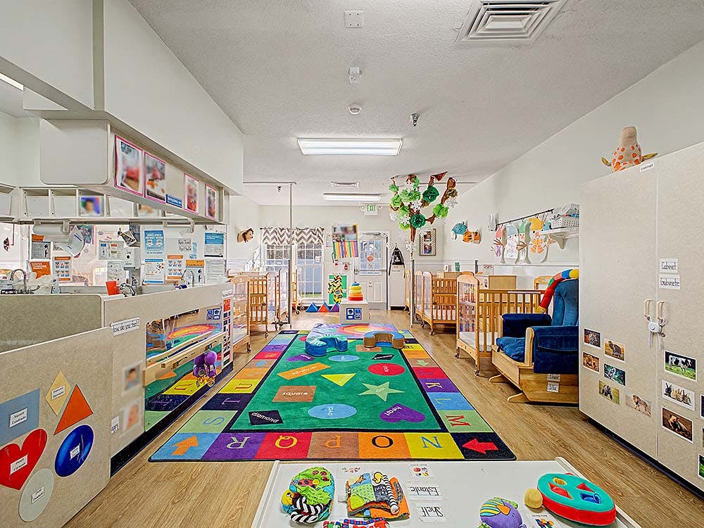 Classroom with cribs, a colorful alphabet rug, and activity tables
