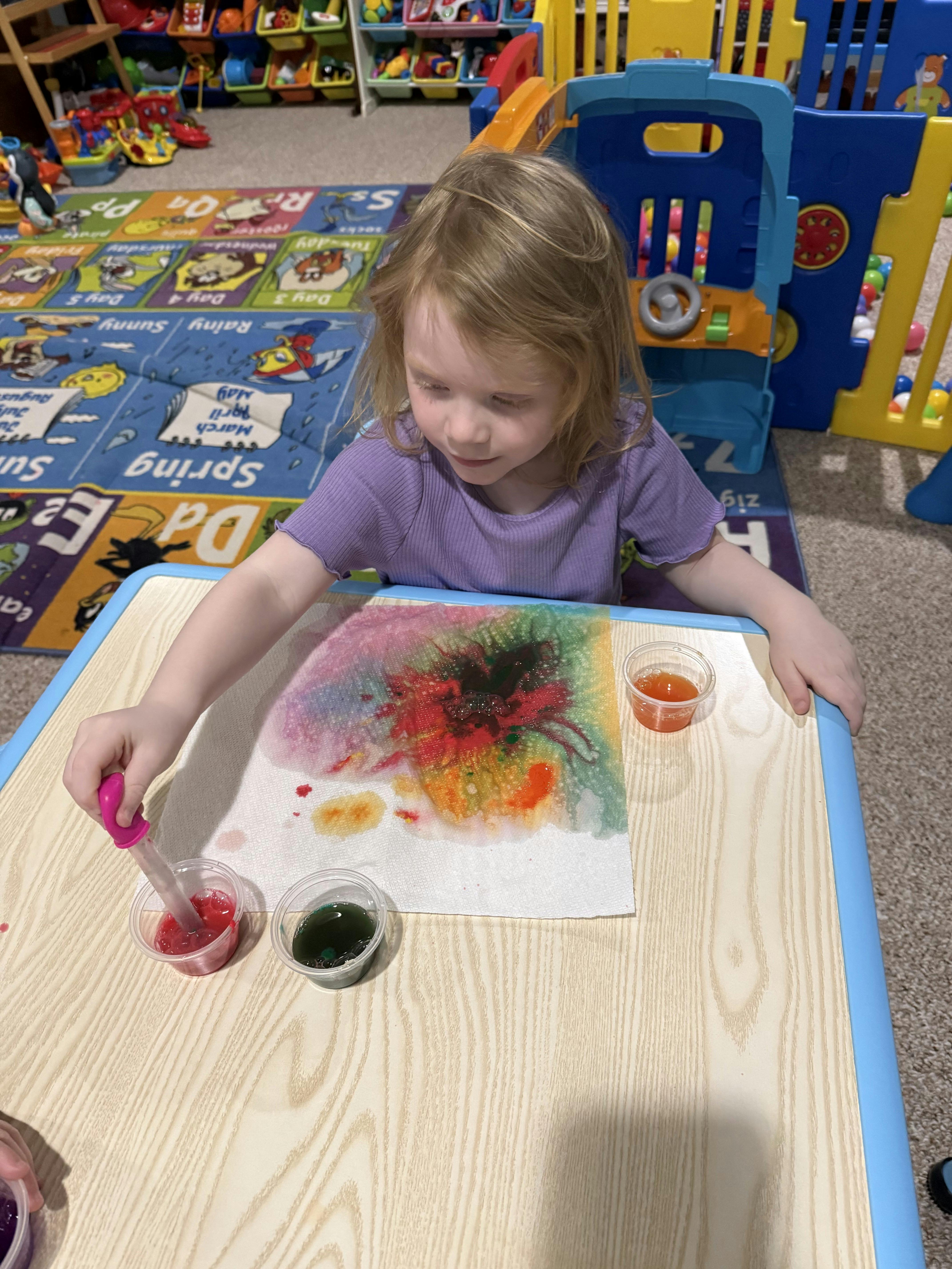 Child using a dropper to put liquid on a paper towel at a play table