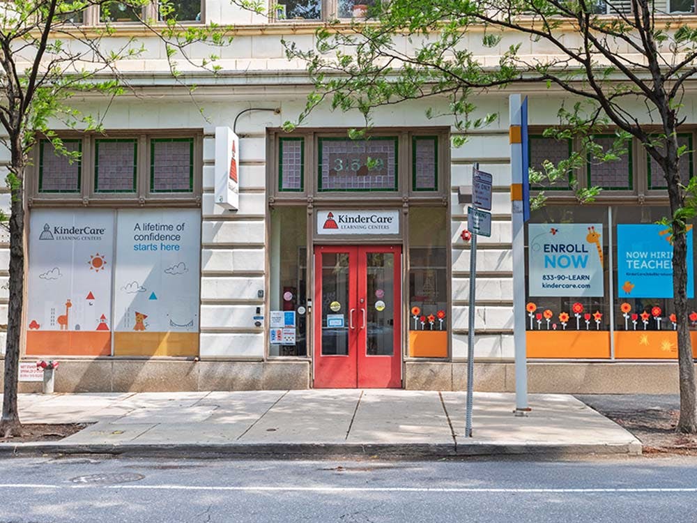 KinderCare Learning Center storefront with "Enroll Now" and "Now Hiring" signs
