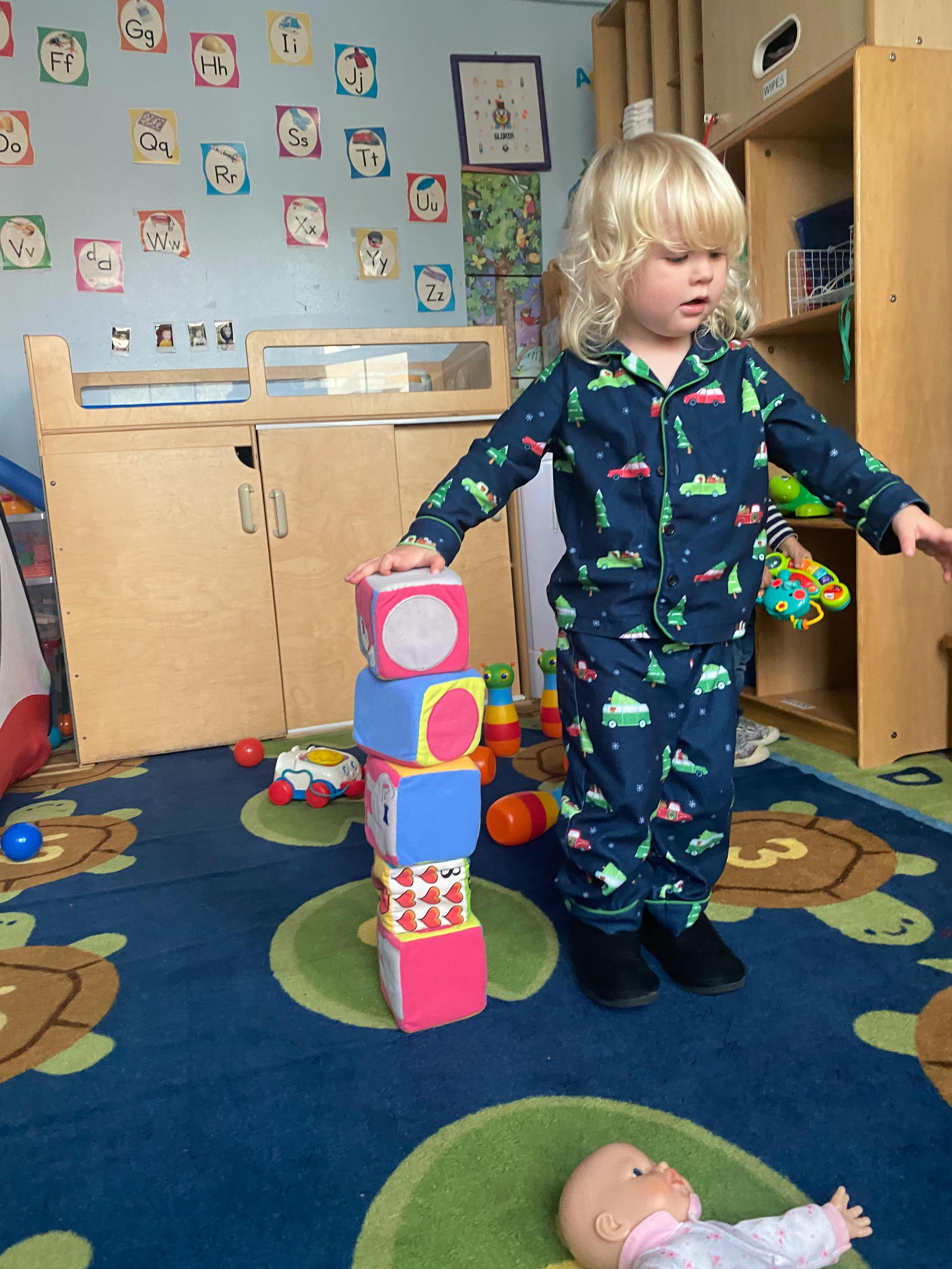 Child in pajamas stacking colorful blocks in a room