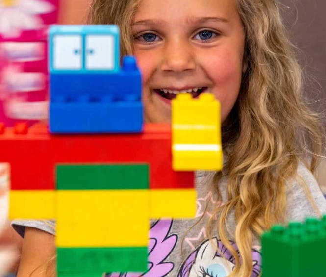 Child smiling behind colorful building blocks
