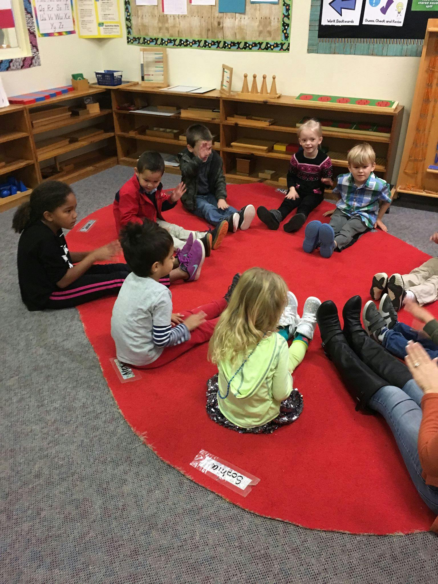 Children sitting on a red rug in a classroom
