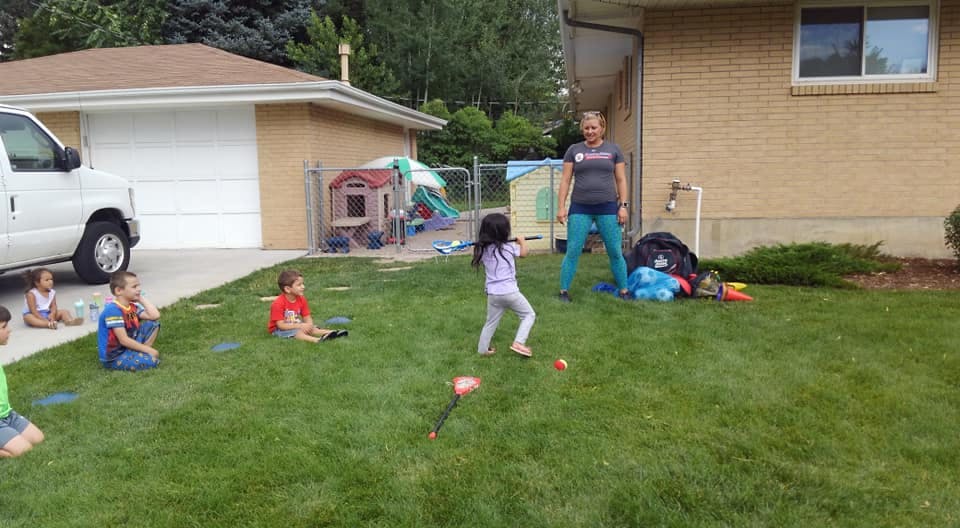 Child playing with a bat and ball while adults and children watch
