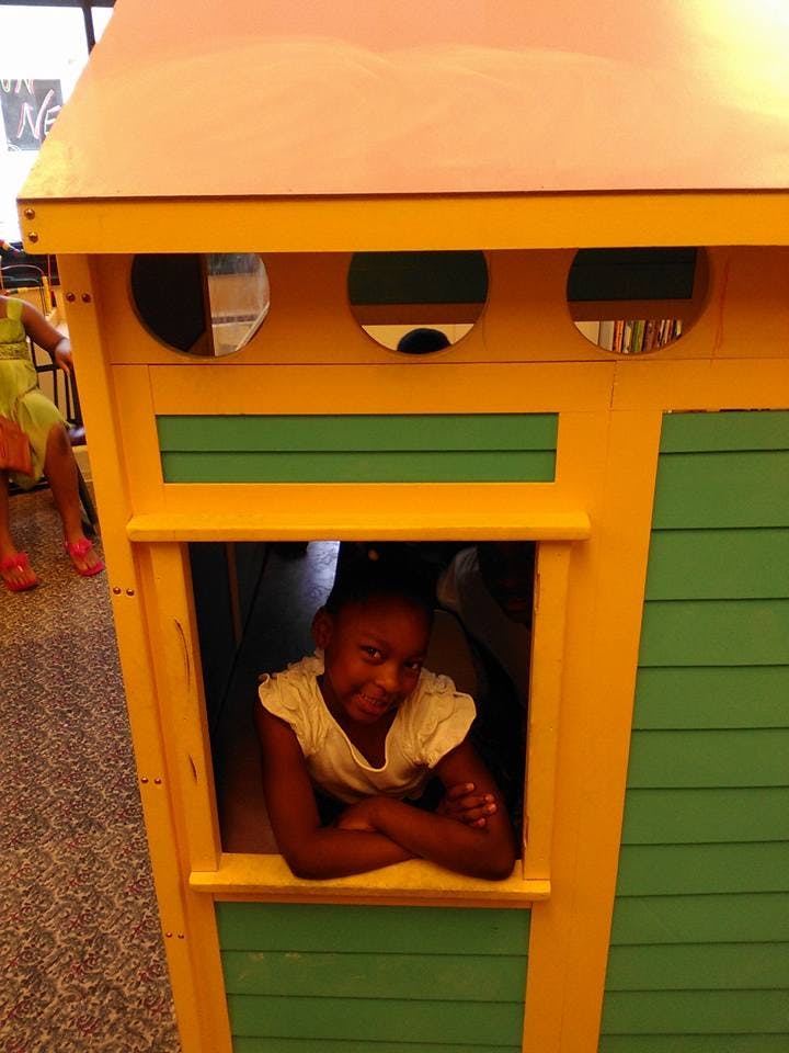 Child looking out of a playhouse window with arms crossed