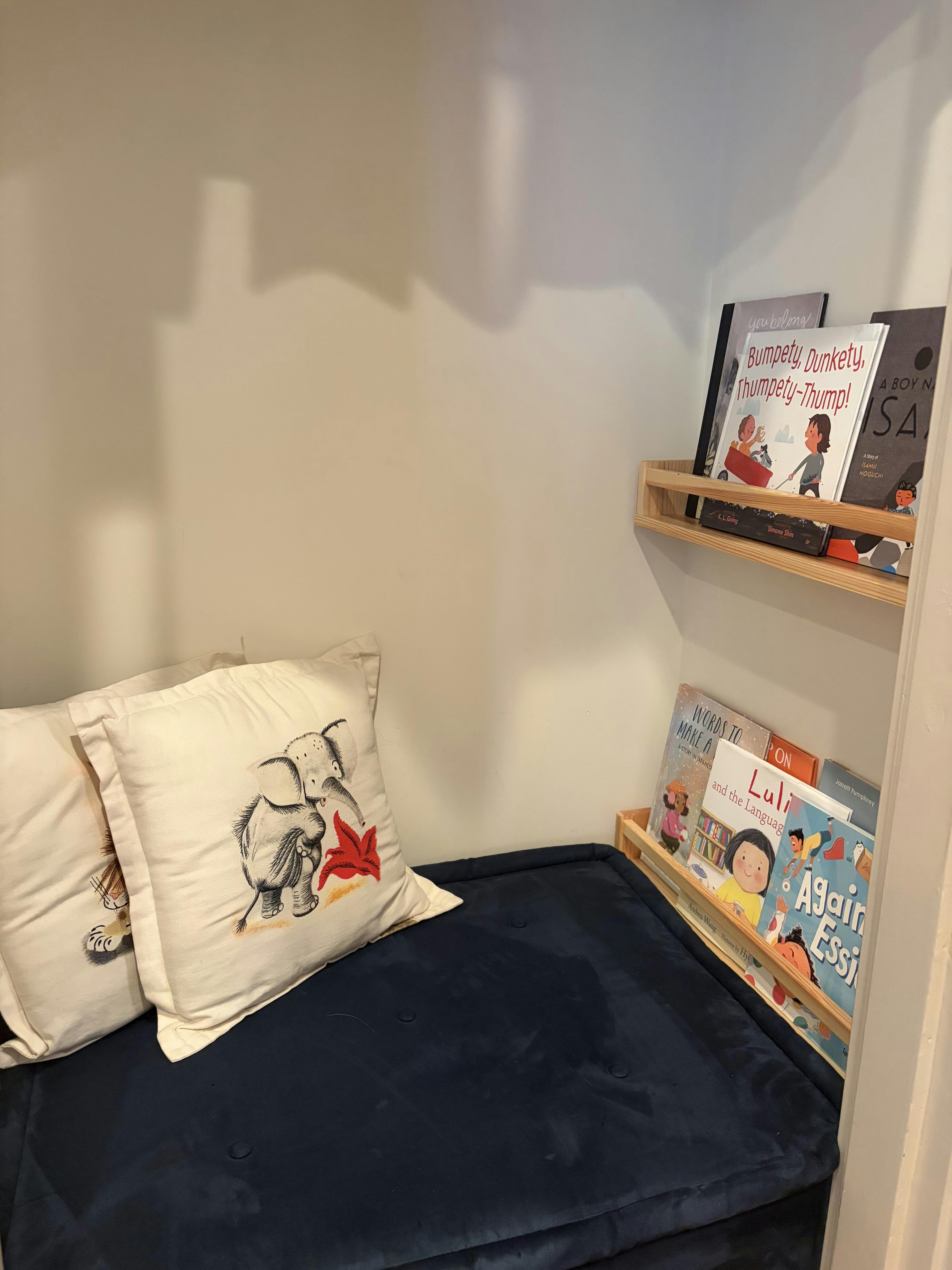 Reading nook with floor cushion pillows and children's books on wall shelves
