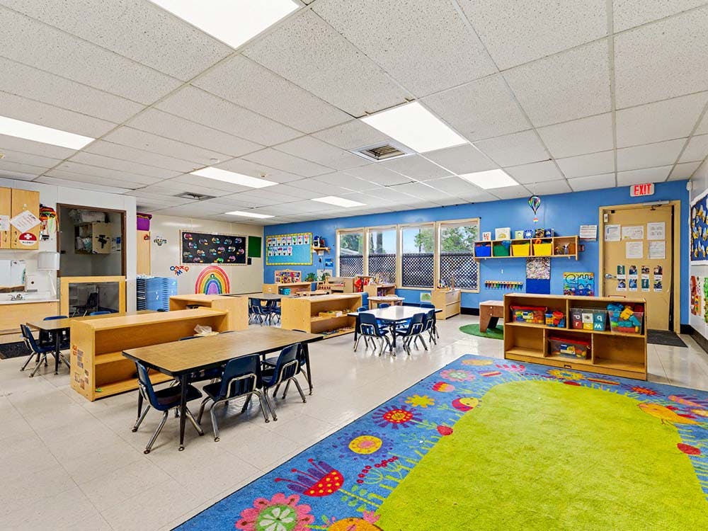 Classroom with tables, chairs, shelves of toys, and a colorful rug