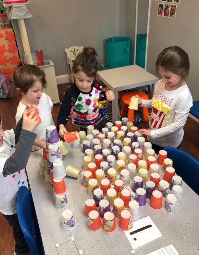 Three children building with colorful cups at a table