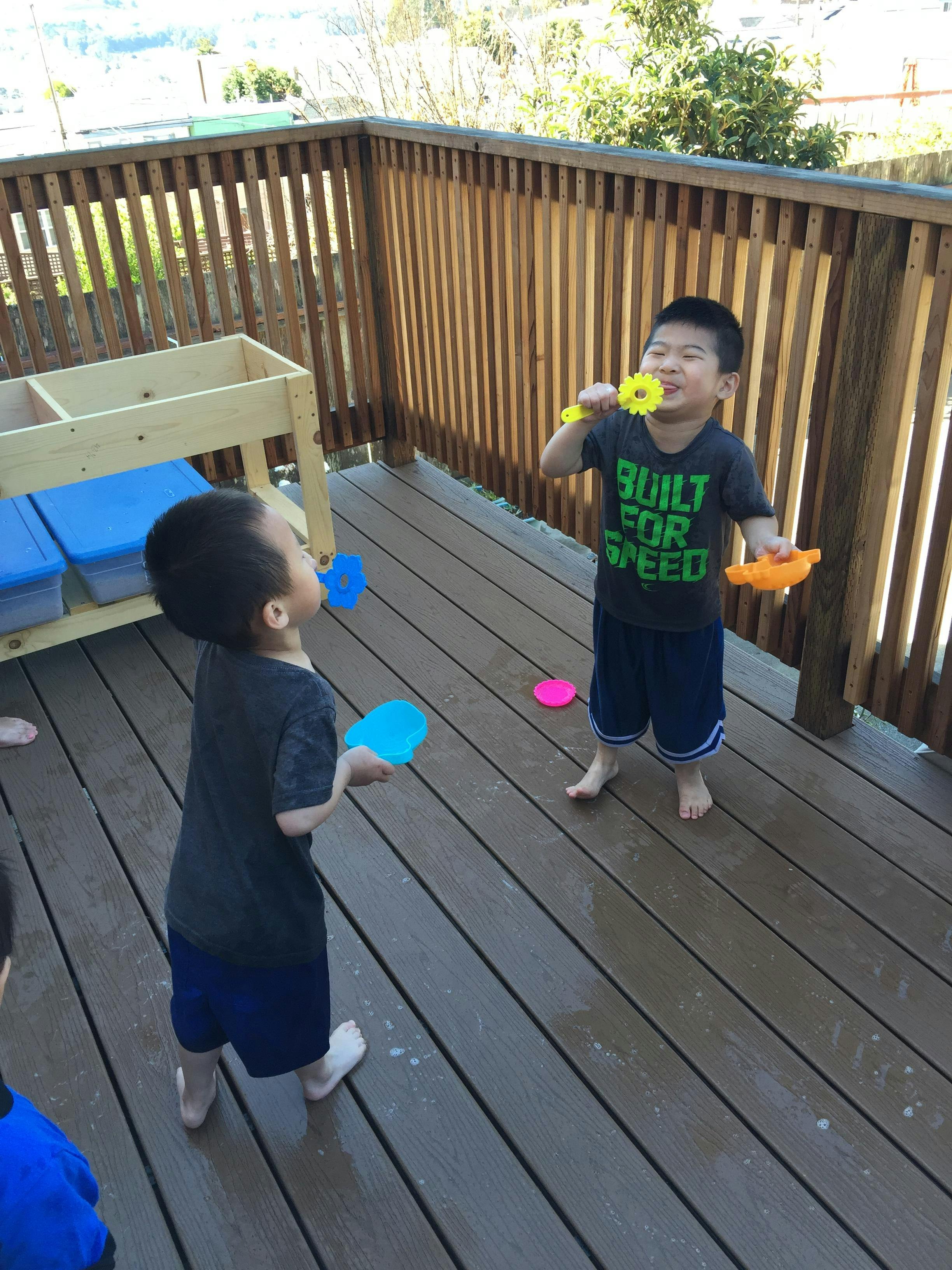 Two children playing with bubble wands on a wooden deck
