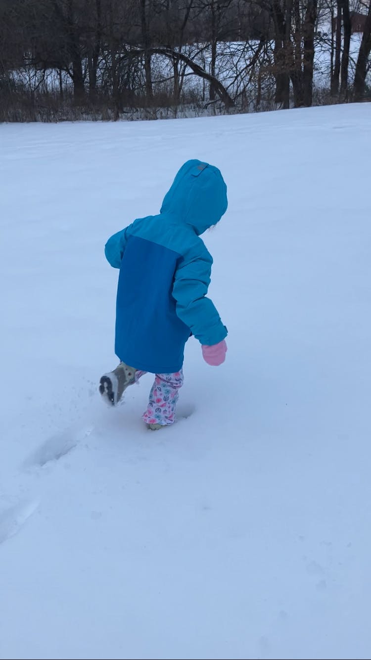Child in a blue coat and pink mittens walking in snow
