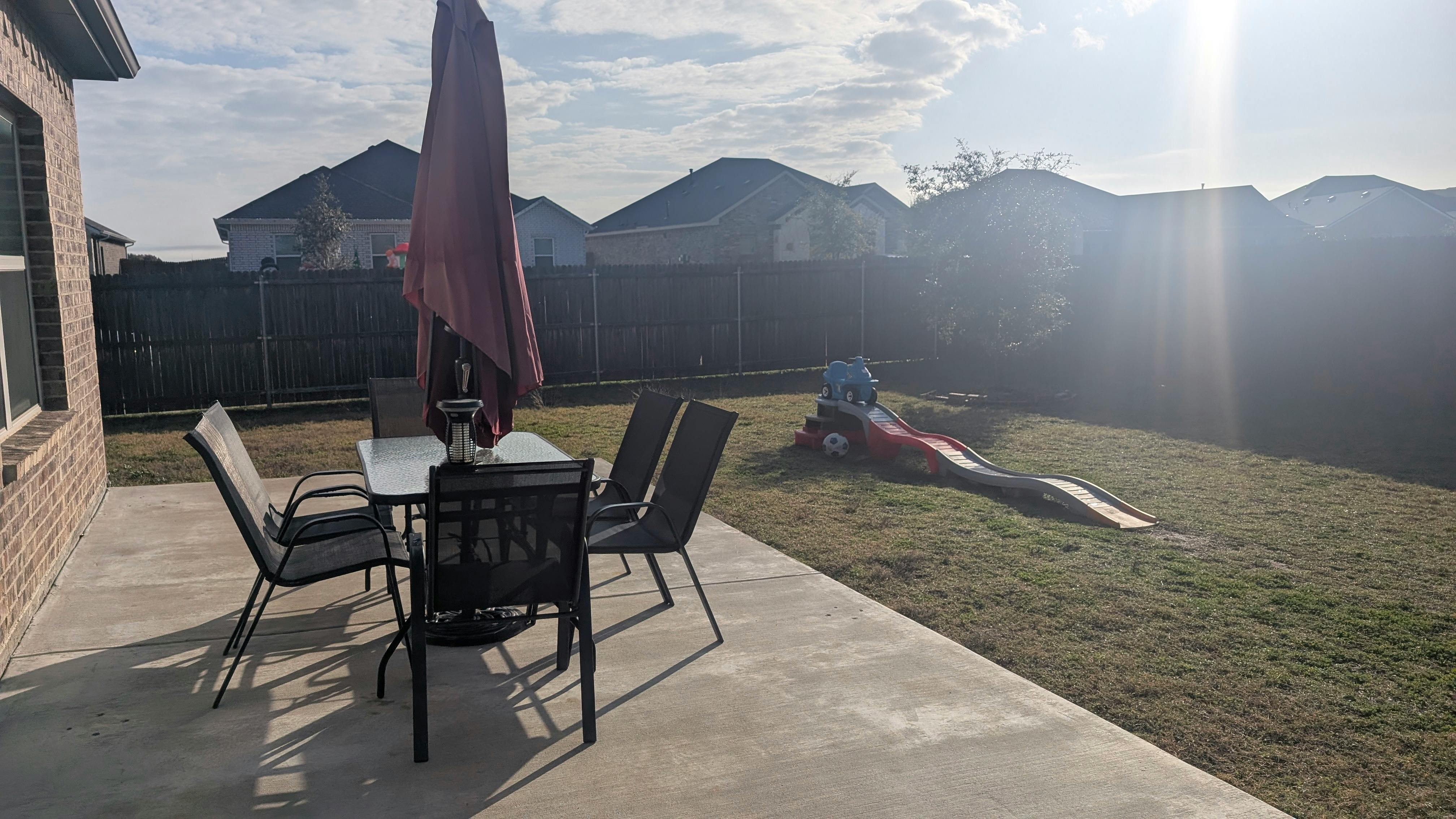 Patio table and chairs with a closed umbrella next to a grassy yard with a slide