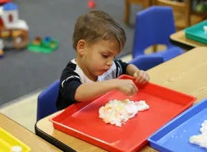 Child playing with white material on a red tray at a table