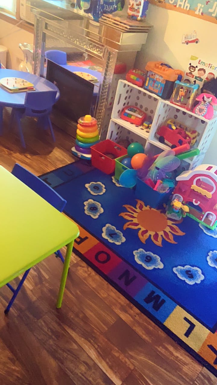Playroom with small tables and chairs, toy shelves, and a sun and cloud rug